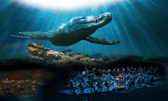 On the bottom right of the image, an orchestra is performing on stage. Behind them is a projection of a still from Life on Our Planet, showing a huge shark appearing to swim towards the audience.